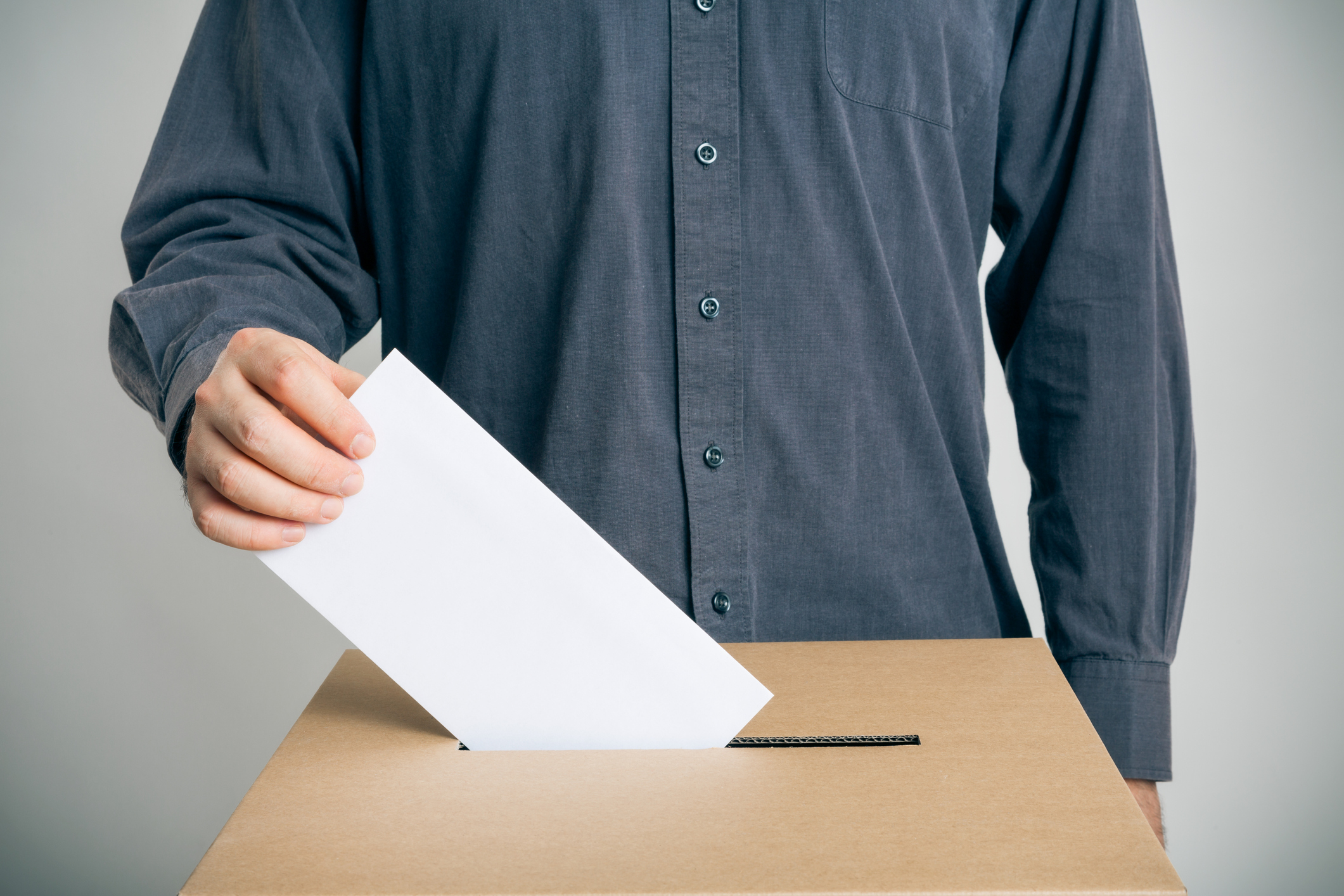 A person placing a ballot into a cardboard voting box